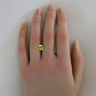 A loose peridot gemstone shown on a woman's hand.