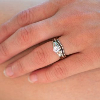 A wooden engagement ring with an interlocking wedding band shown from above on a finger