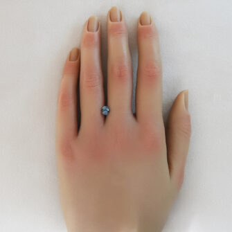 A blue-green color change sapphire shown on a woman's hand.