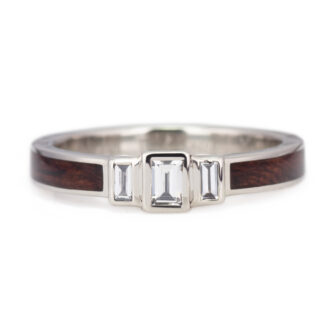 A front-on view of a modern three-stone engagement ring featuring three baguette-cut diamonds set in 14k white gold with a distinctive wood inlay band.