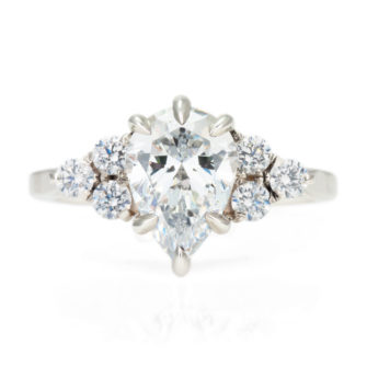 A picture of a pear cut moissanite engagement ring with a lab-grown diamond cluster.