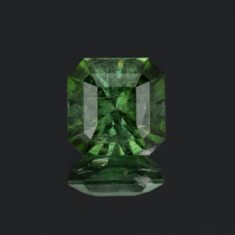 An photograph of a square cut forest-green tourmaline, moderately included.