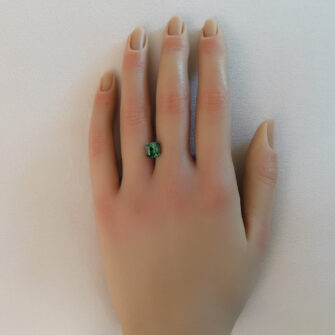 A forest green square cut tourmaline shown on a hand.