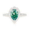 An image of a white gold moissanite engagement ring with a green pear cut center stone.